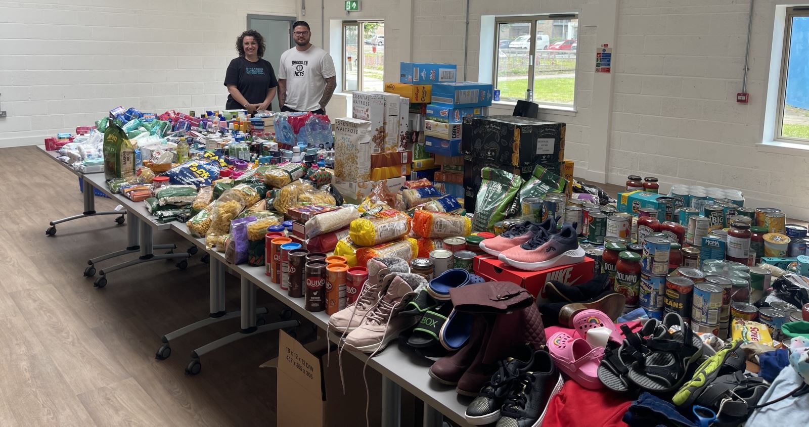 Two people stood next to a table of donated food and items